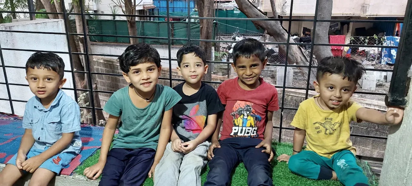 Five young boys sitting together outdoors on the green mat at Maza Ghar